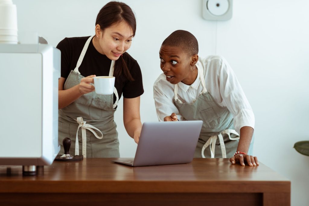 positive waitresses working on laptop and discussing work