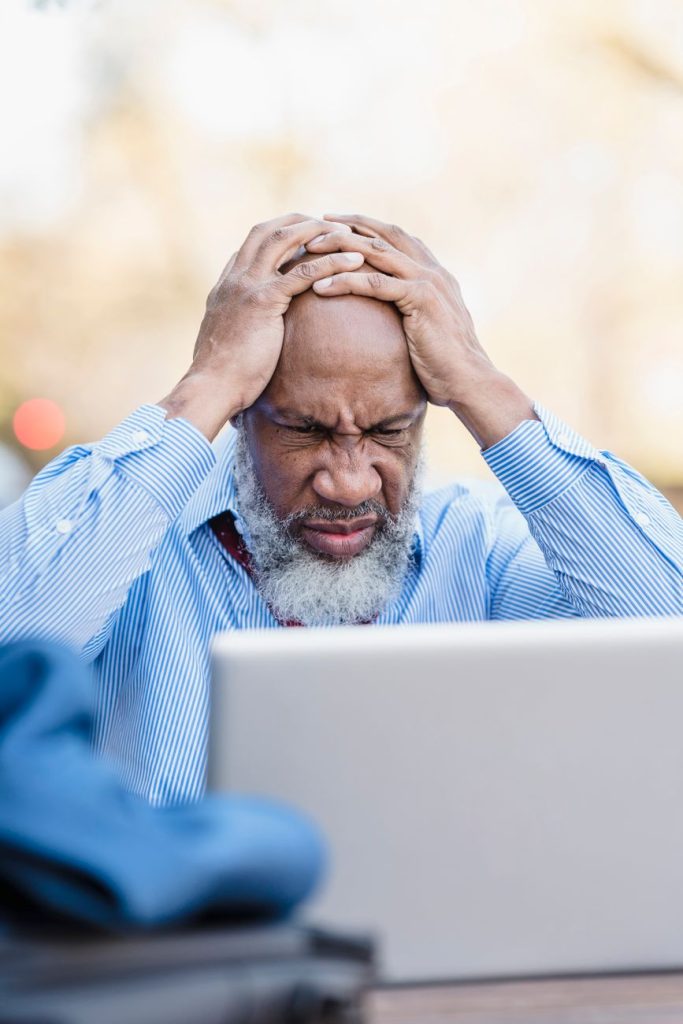a man with his hands on his head while looking at his laptop